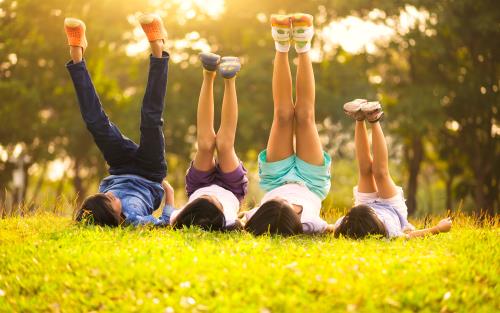 Fyra barn ligger i gräset på rygg och sträcker upp benen mot himlen.