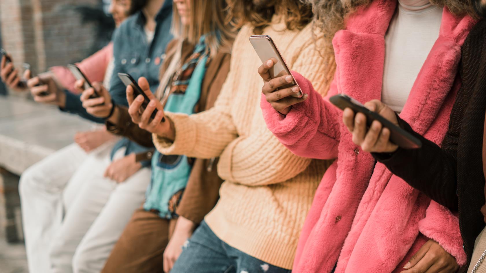 Ett gäng ungdomar står på rad med sina mobiltelefoner i handen.