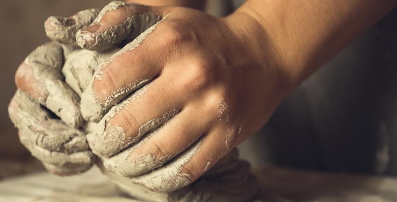 Ett par händer knådar lera på ett arbetsbord.