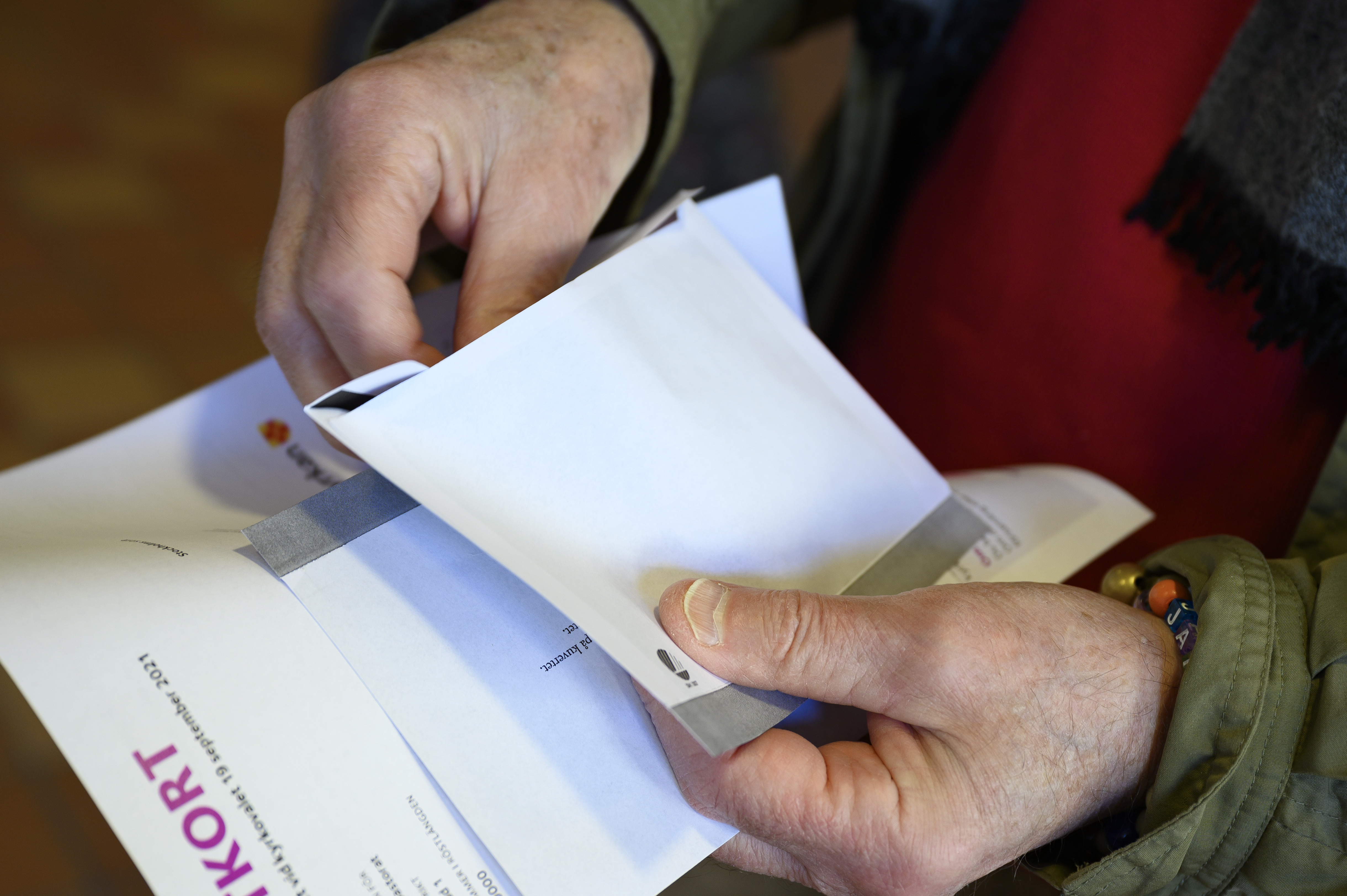 En person står med sitt röstkort och valkuvert i händerna.