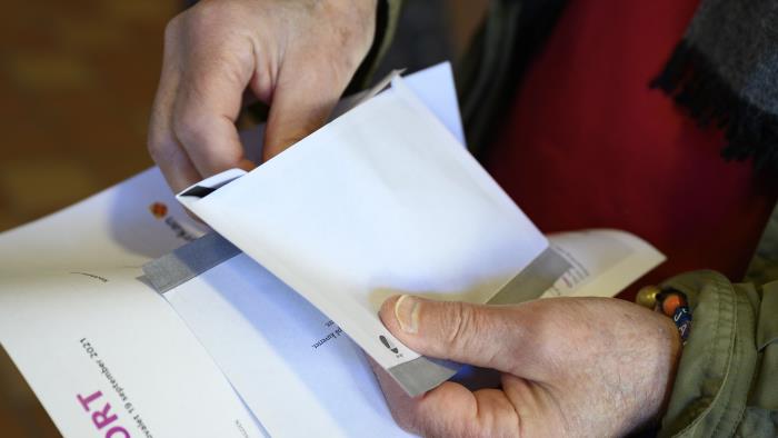 En person står med sitt röstkort och valkuvert i händerna.
