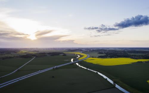 Flygfoto över en bilväg och en å genom ett fält.