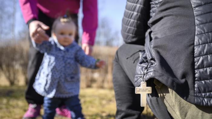 En bebis på vårpromenad får hjälp att lära sig gå av sina föräldrar.