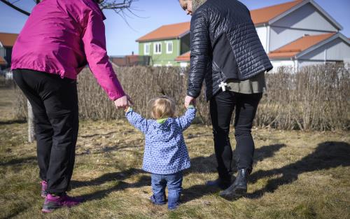 Ett litet barn på vårpromenad håller sina föräldrar med bägge händerna för att inte ramla omkull.