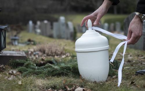 Någon knyter ett vitt band runt en vit urna på en kyrkogård.