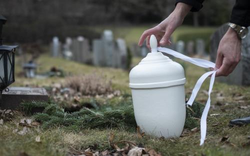 Någon knyter ett vitt band runt en vit urna på en kyrkogård.