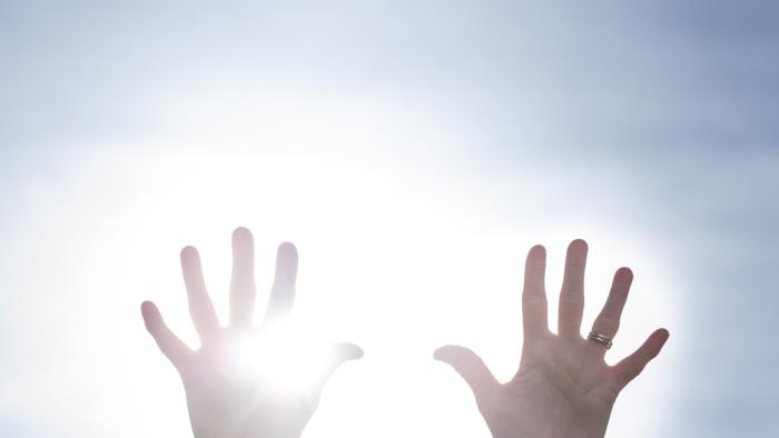 Två händer uppsträckta mot en blå himmel. Solen lysen mellan fingrarna.