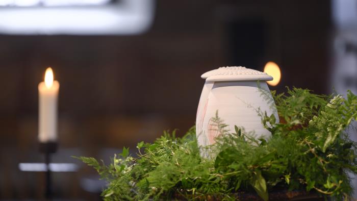 Två urnor står bland ormbunksblad på ett bord i kyrkan.