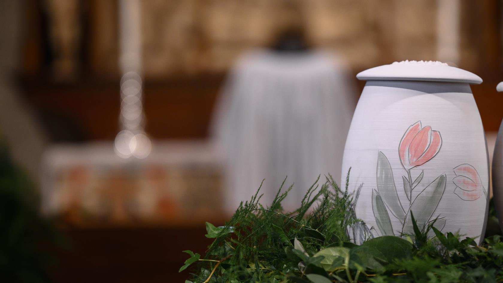 En urna med handmålade tulpaner står bland ormbunksblad på ett bord i kyrkan. En präst syns längre bort.