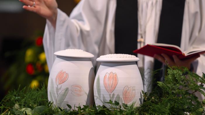Två urnor med handmålade tulpaner står bland ormbunksblad på ett bord i kyrkan. En präst står bakom.