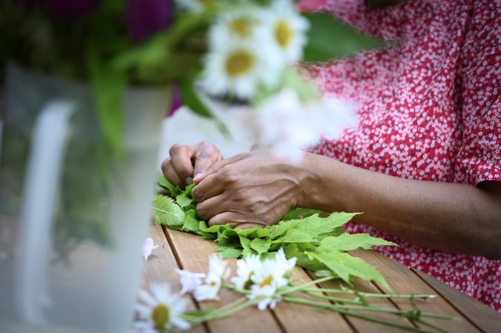 En kvinna sitter vid ett bord och knyter en blomsterkrans.