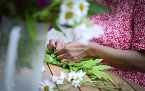 En kvinna sitter vid ett bord och knyter en blomsterkrans.