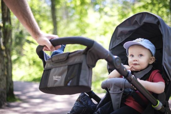 En bebis med keps i barnvagn är på promenad i skogen.