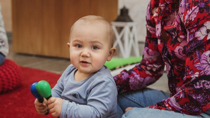 En bebis sitter på golvet framför sin mamma och spelar maraccas.