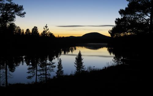 Skog och ett berg reflekteras på en stilla vattenyta i solnedgången.