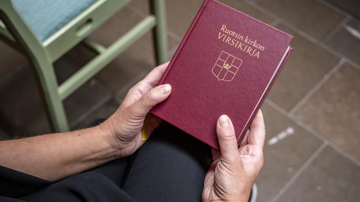Någon sitter i ett kapell och håller en finsk psalmbok i händerna.
