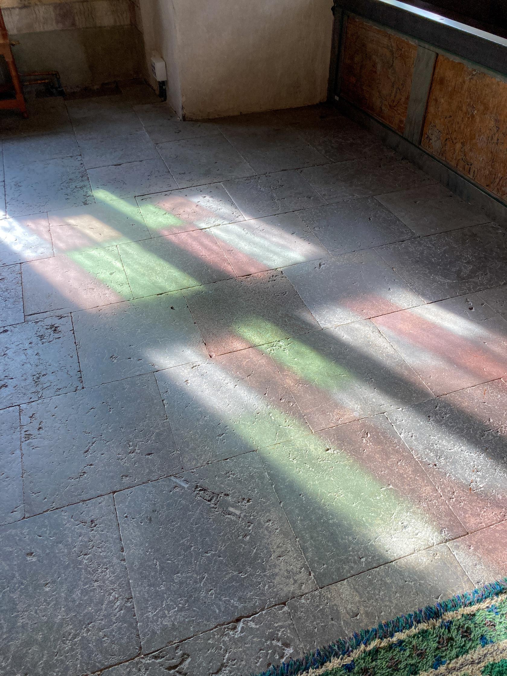 Ljuset från ett färggrant kyrkfönster reflekteras mot stengolvet i en kyrka.