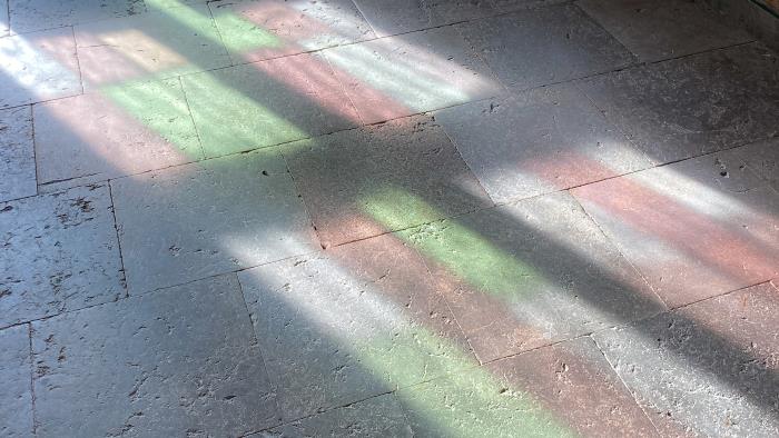 Ljuset från ett färggrant kyrkfönster reflekteras mot stengolvet i en kyrka.
