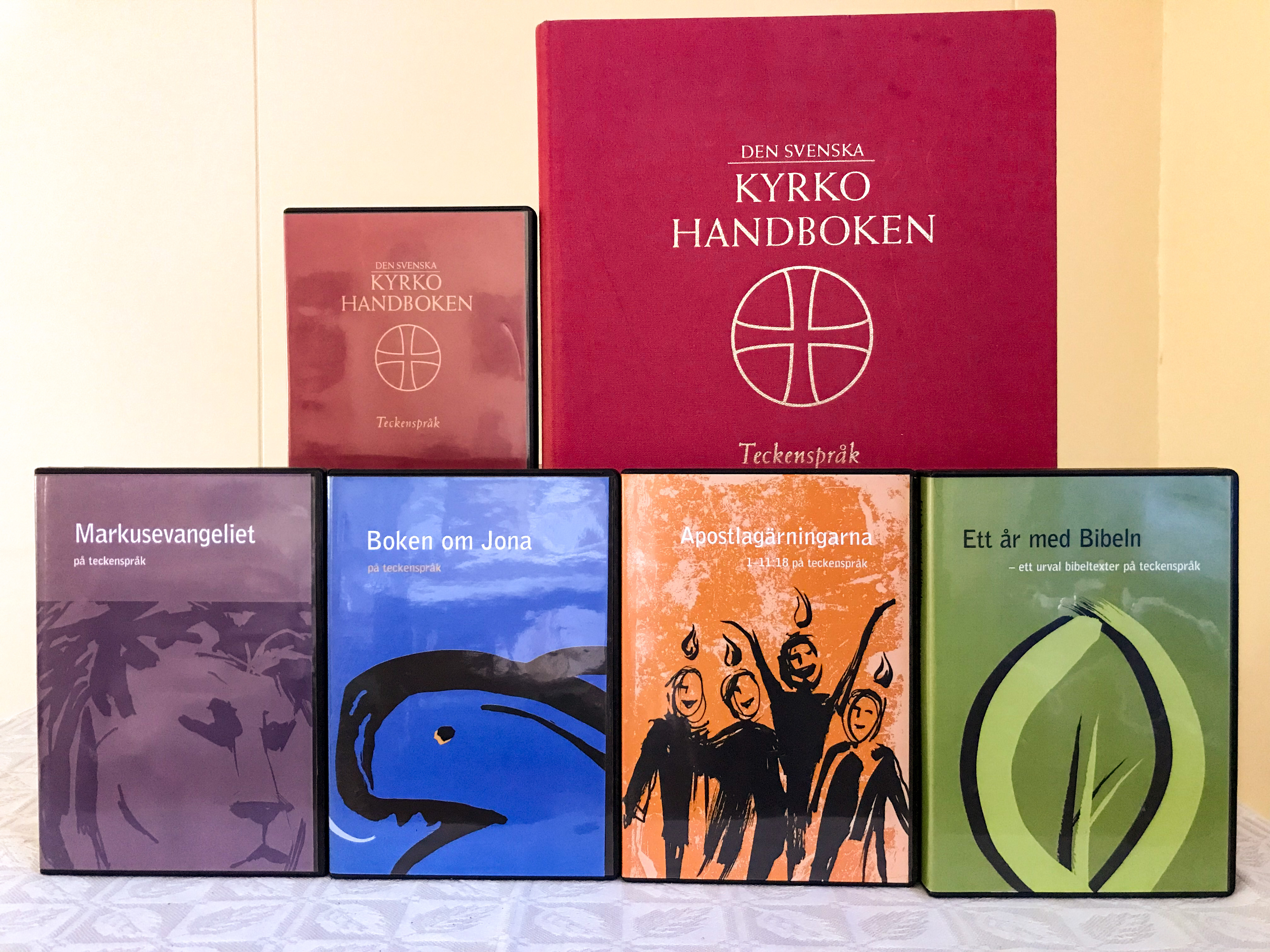 Delar av bibeln och kyrkohandboken på teckenspråk och som ljudböcker står uppställda på ett bord.