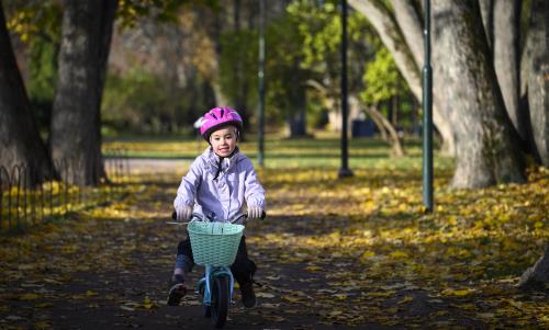 Ett barn med rosa hjälm cyklar genom en park full av höstlöv på marken.