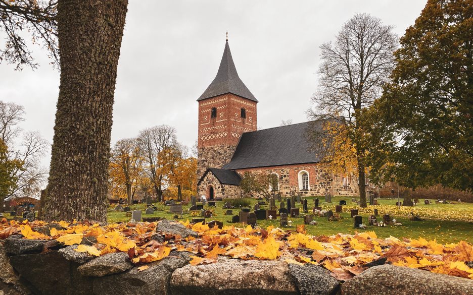Exteriörbild av Skepptuna kyrka. I förgrunden syns gula höstlöv.