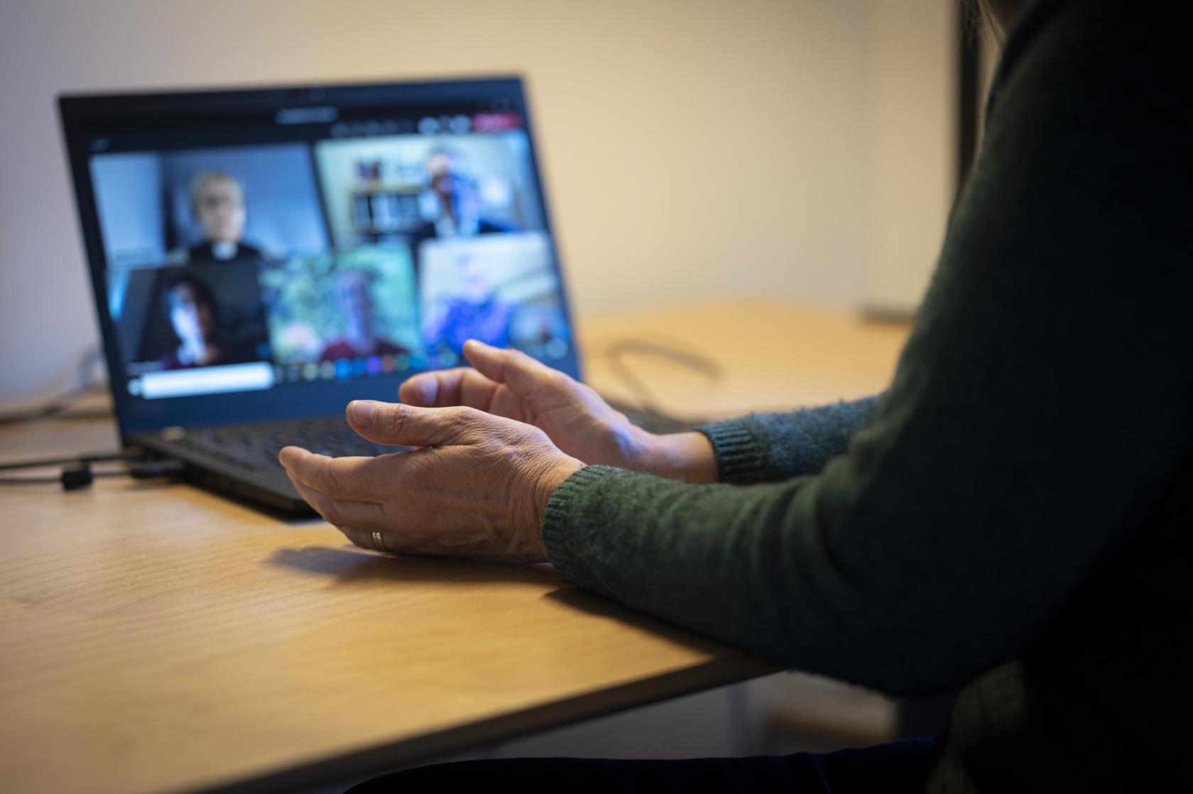 En person sitter vid ett skrivbord och har ett digitalt möte i datorn med några andra.