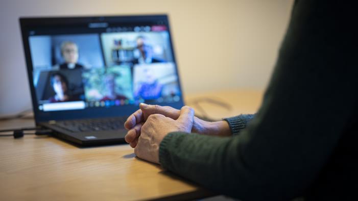 En person sitter vid ett skrivbord och har ett digitalt möte i datorn med några andra.