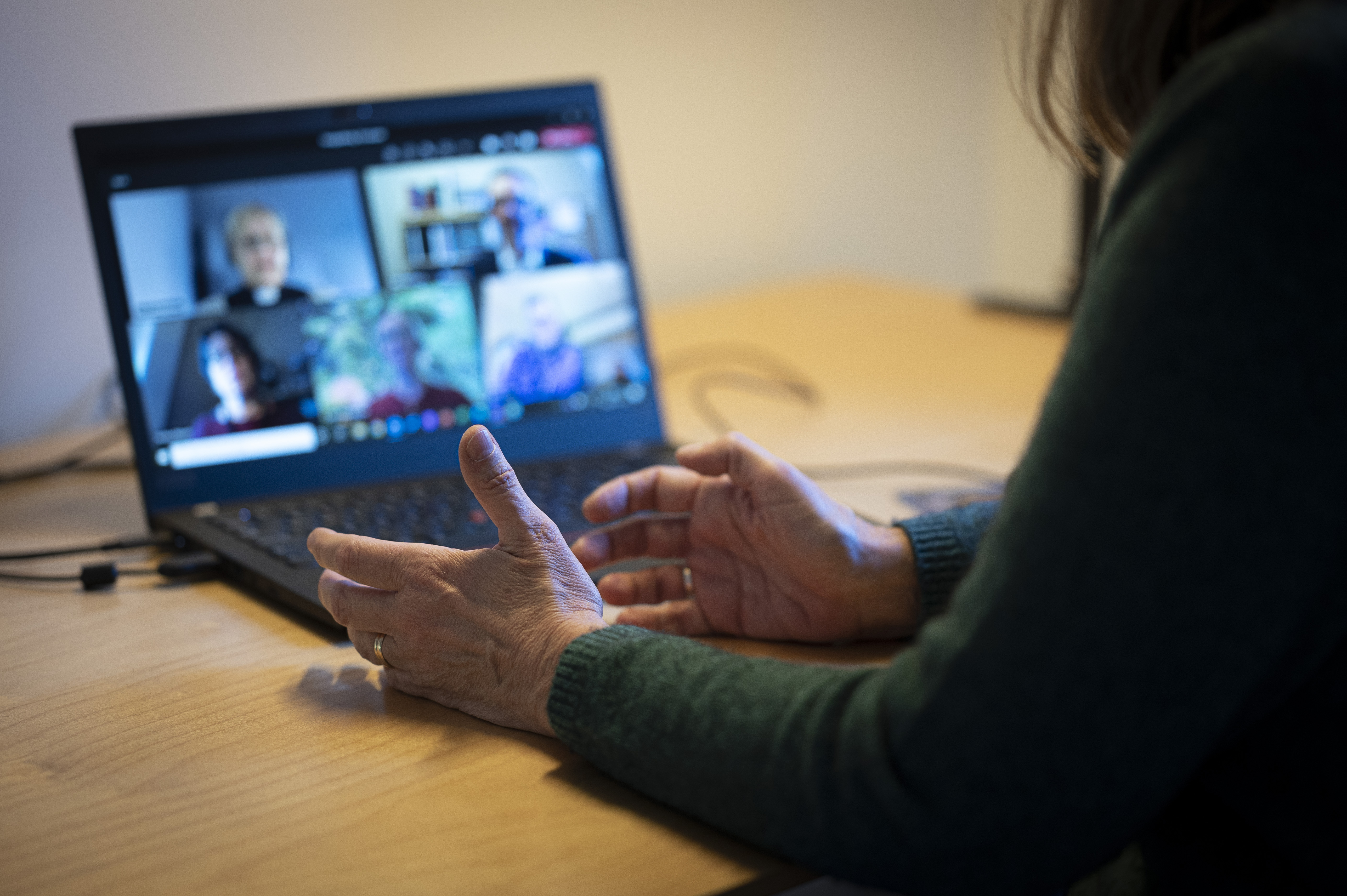 En person sitter vid ett skrivbord och har ett digitalt möte i datorn med några andra.