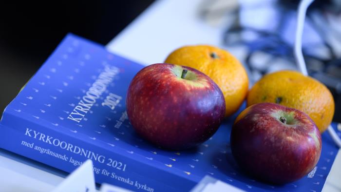 Två äpplen och två clementiner ligger på en blå bok med titeln Kyrkoordning 2021.