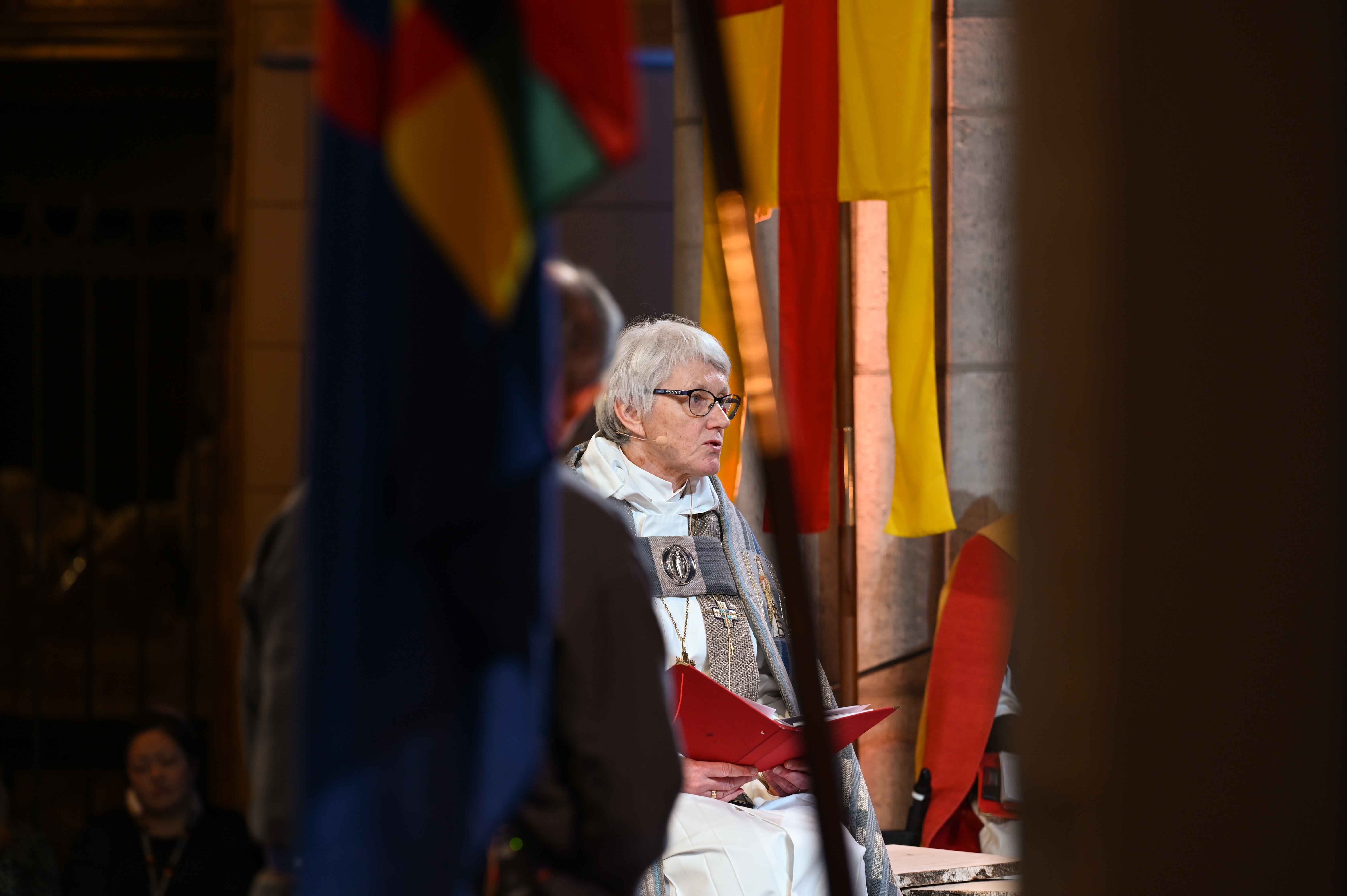 Ärkebiskop Antje Jackelén läser högt i Uppsala domkyrka omgiven av Svenska kyrkans och den samiska flaggan.