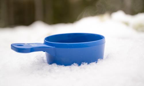 Närbild på en blå kåsa nedtryckt i snön.