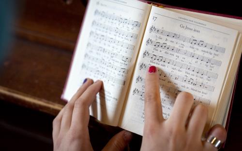 En person med målade naglar följer med sitt pekfinger melodin i en uppslagen psalmbok.