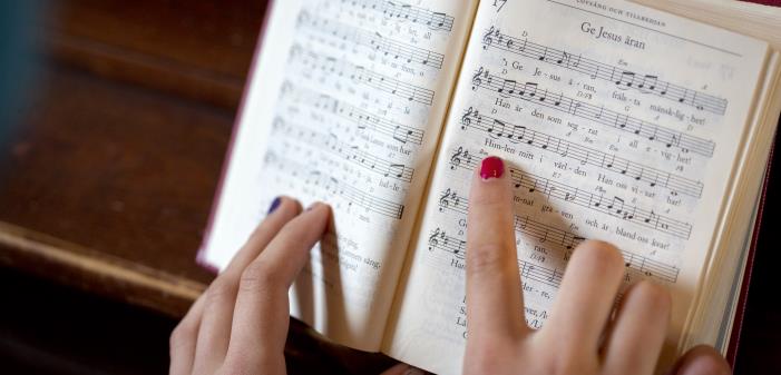 En person med målade naglar följer med sitt pekfinger melodin i en uppslagen psalmbok.