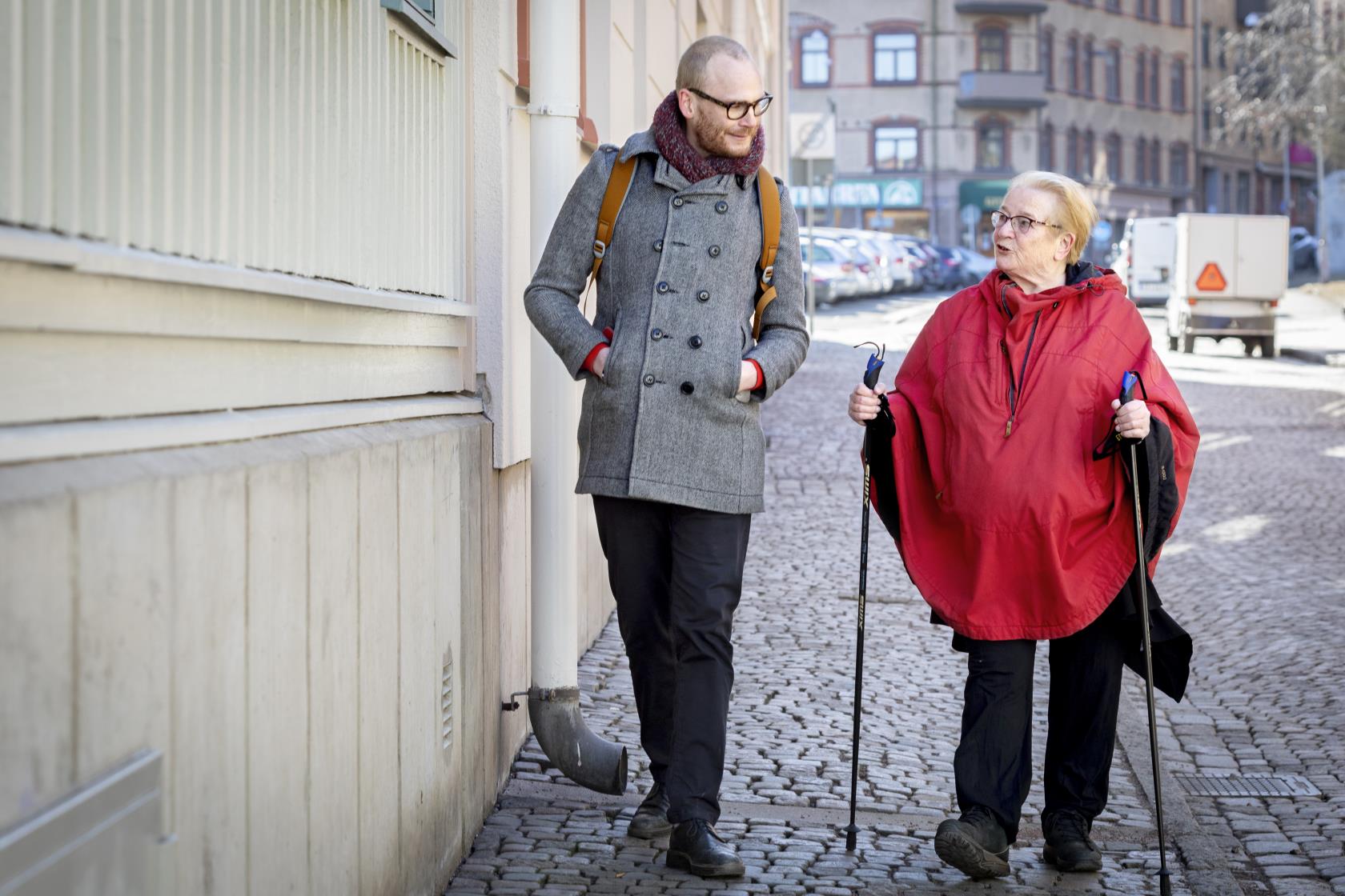 Än äldre kvinna med stavar är ute och promenerar på stan tillsammans med en ung man.