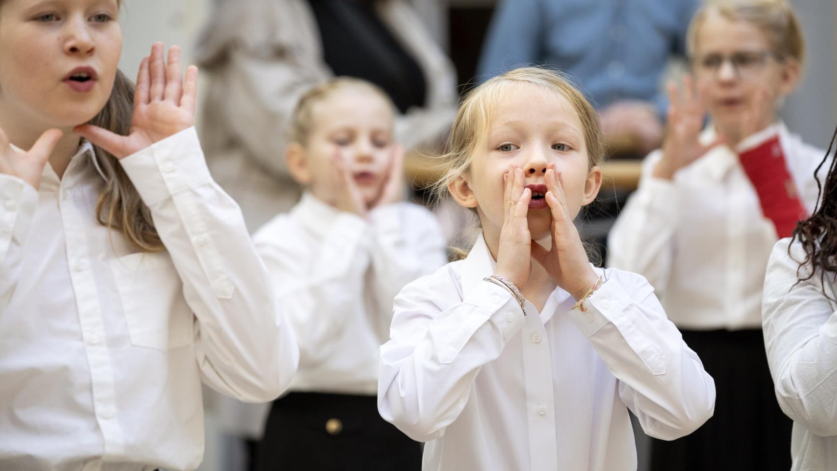 Medlemmar i en barnkör står och sjunger i en kyrka. De håller händerna framför munnen som en tratt.