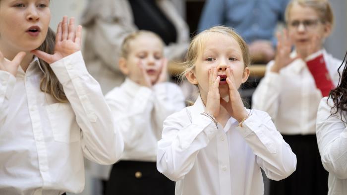 Medlemmar i en barnkör står och sjunger i en kyrka. De håller händerna framför munnen som en tratt.