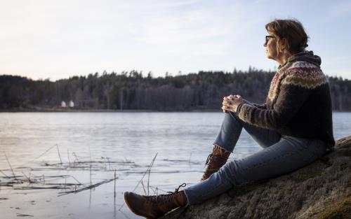 En kvinna sitter på en klippa och tittar ut över vattnet.