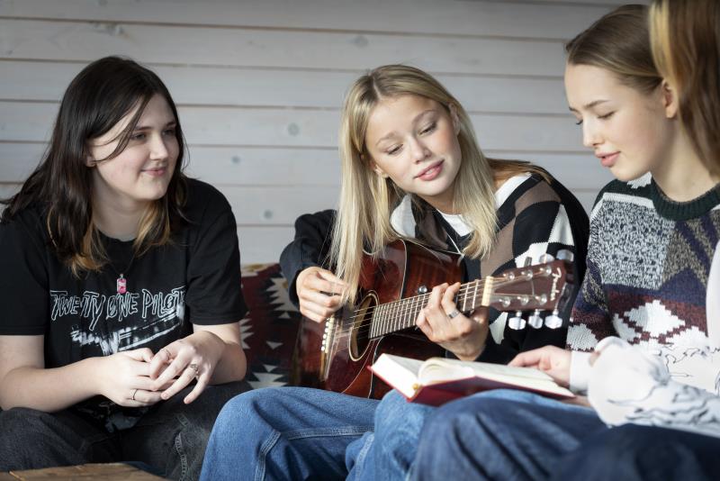 Några tonårstjejer sitter och sjunger och spelar gitarr.
