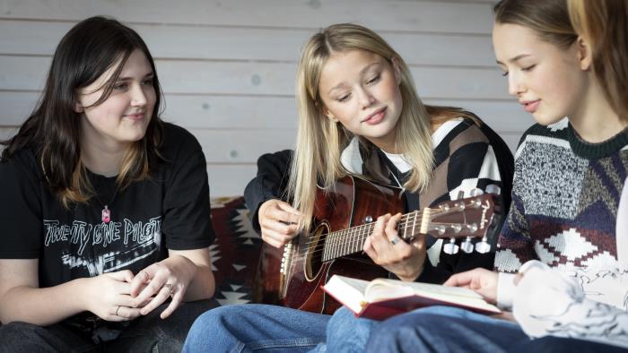 Några tonårstjejer sitter och sjunger och spelar gitarr.