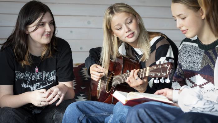 Några tonårstjejer sitter och sjunger och spelar gitarr.