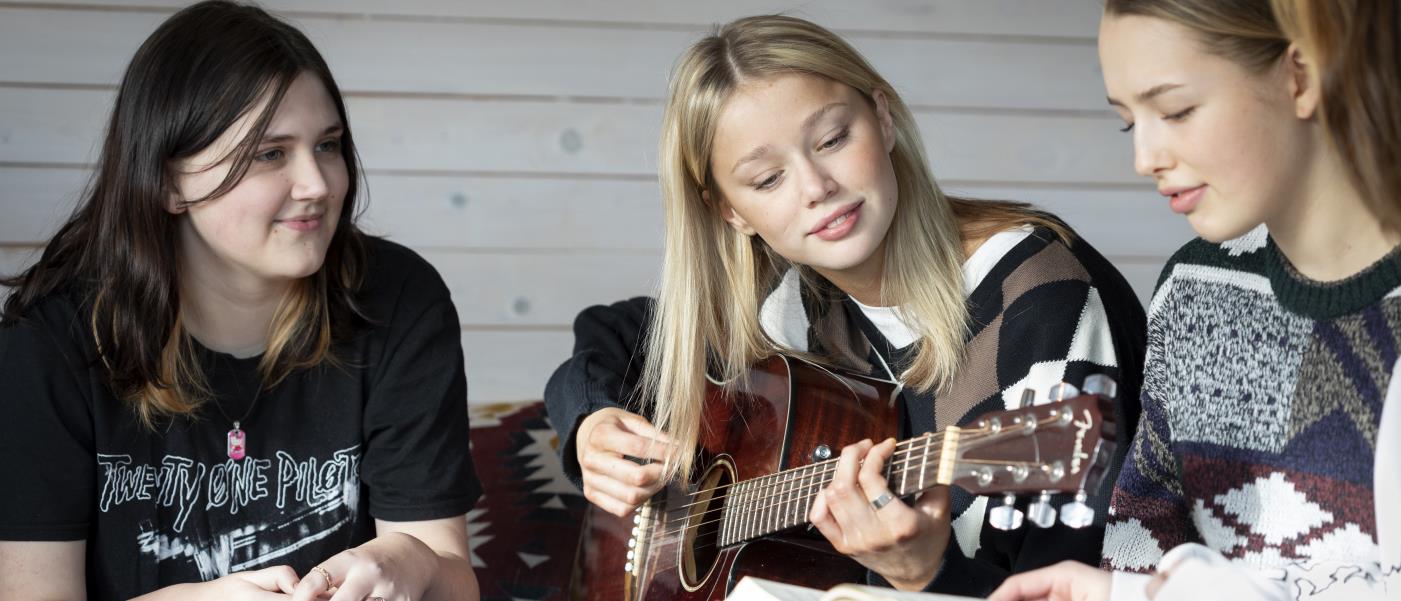 Några tonårstjejer sitter och sjunger och spelar gitarr.