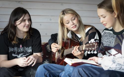 Några tonårstjejer sitter och sjunger och spelar gitarr.