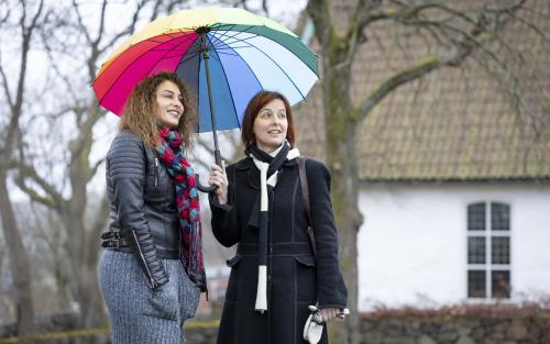Två kvinnor står under ett färgglatt paraply.