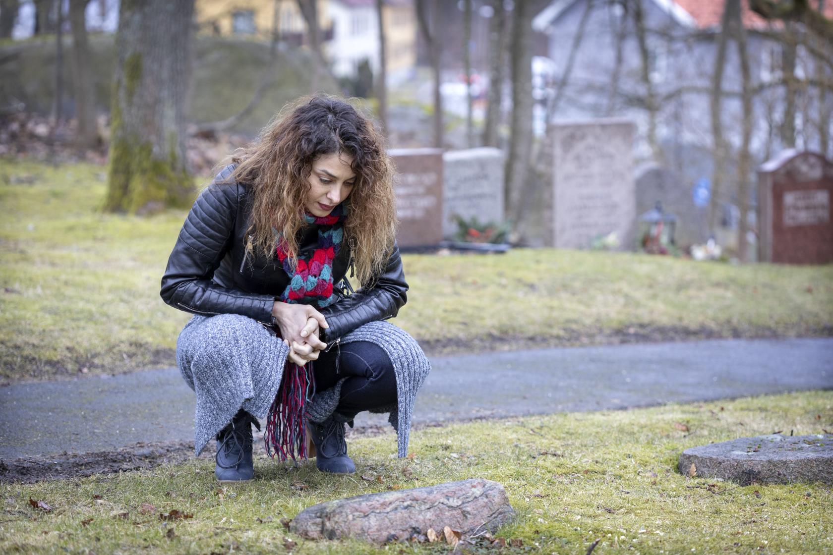 En kvinna på en kyrkogård sitter på huk vid en minnessten.