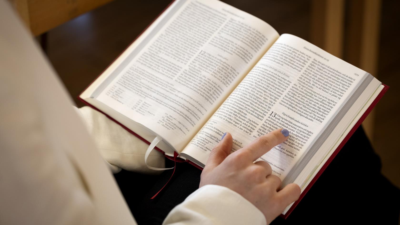Någon läser ur en bibel och följer texten med fingret.