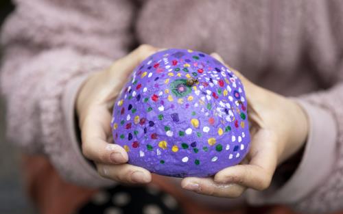 När bild på någon som håller upp en halvklot-formad sten som målats lila och med en massa olikfärgade prickar.