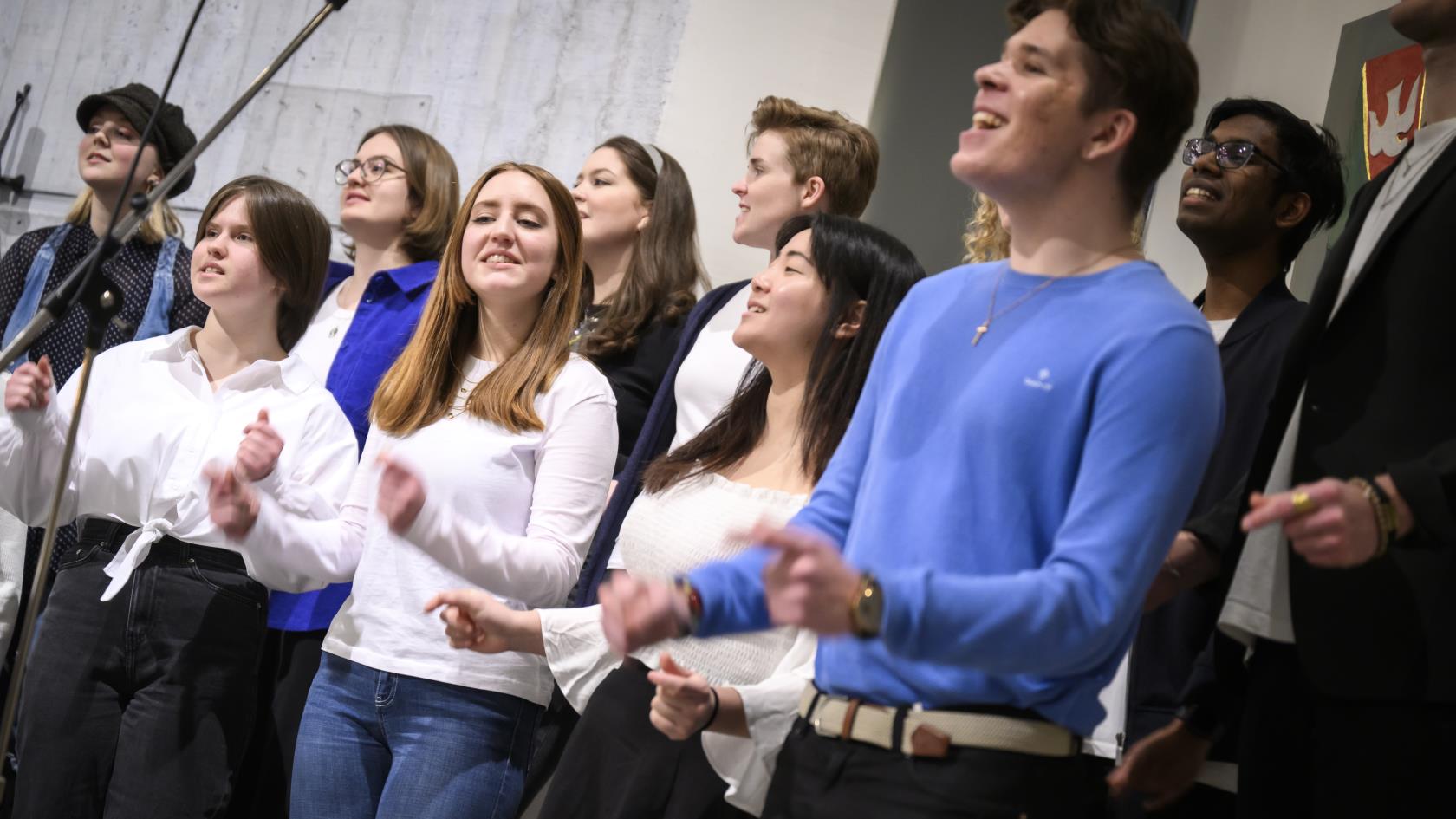 En blandad ungdomskör sjunger och klappar händer i en kyrka.