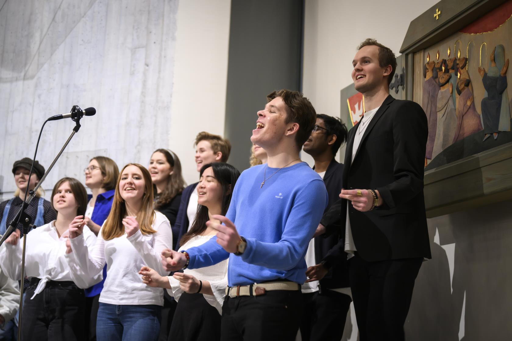 En blandad ungdomskör sjunger och klappar händer i en kyrka.