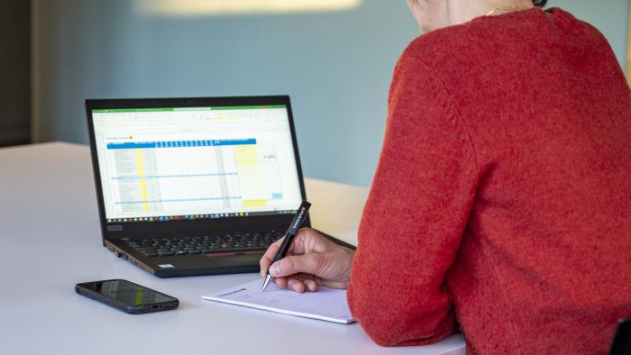 En kvinna sitter vid ett bord med en laptop och ett block framför sig.