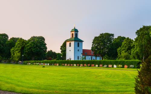 En vit landsbygdskyrka bland lummiga träd.